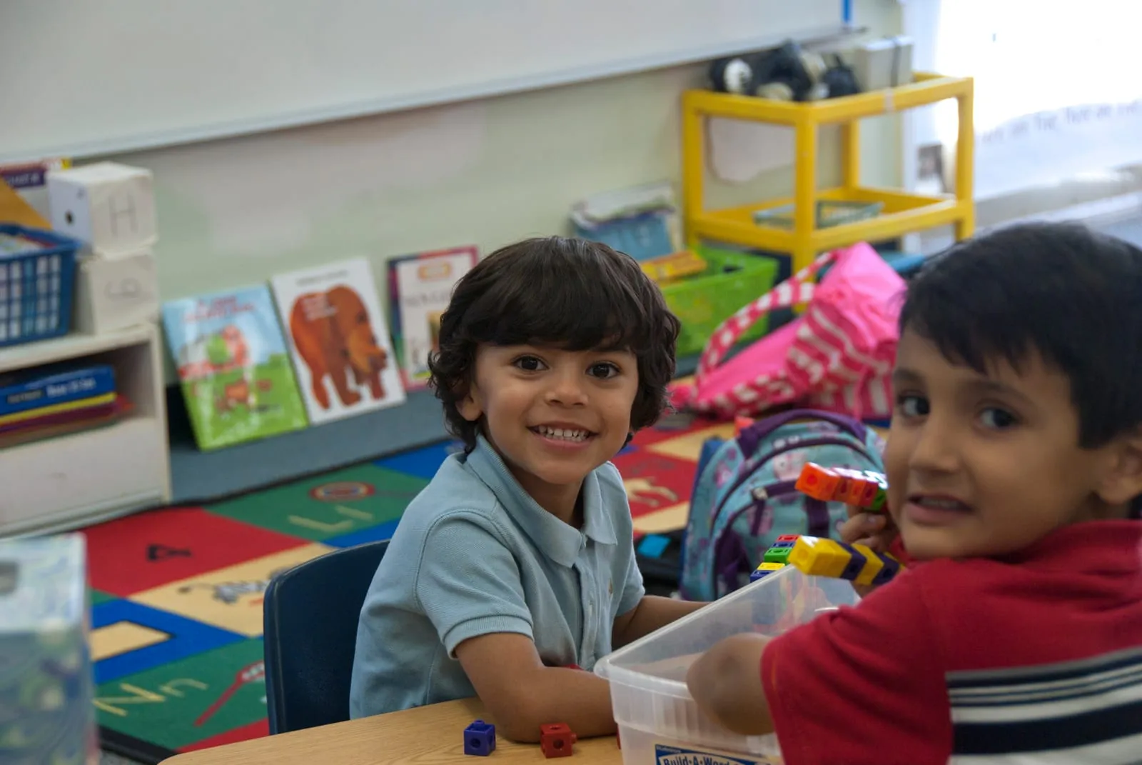 Dos alumnos de jardín sonriendo en el aula, jugando con bloques sobre la mesa.