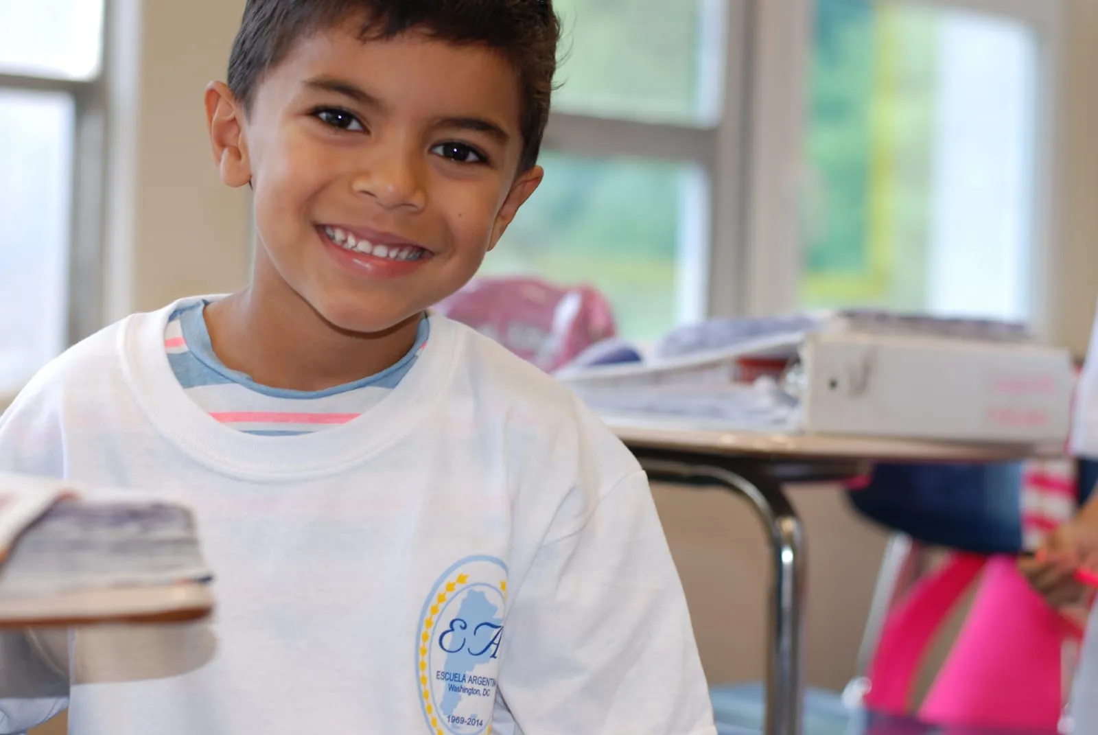 Un alumno de primaria sonriendo en el aula, con su remera de la Escuela.