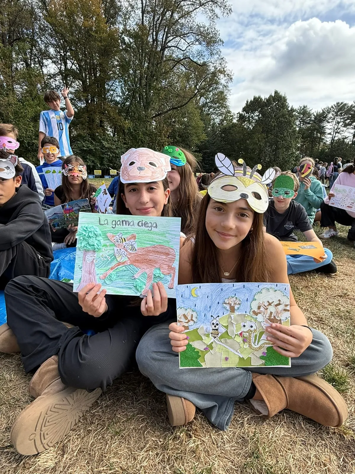 Dos alumnas muestran sus trabajos ilustrados, sentadas en el pasto.