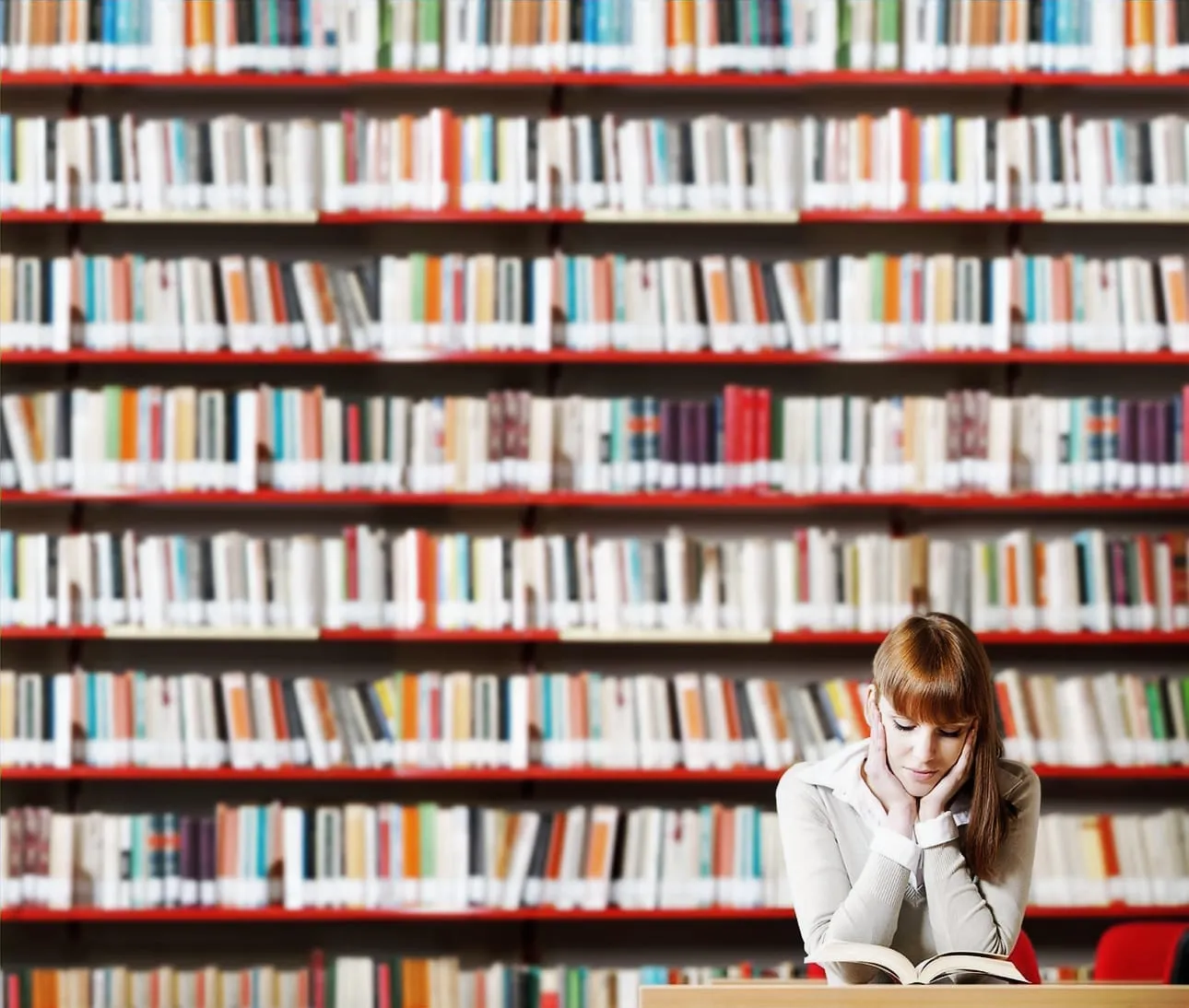 Una alumna leyendo en una mesa frente a los estantes de la biblioteca.