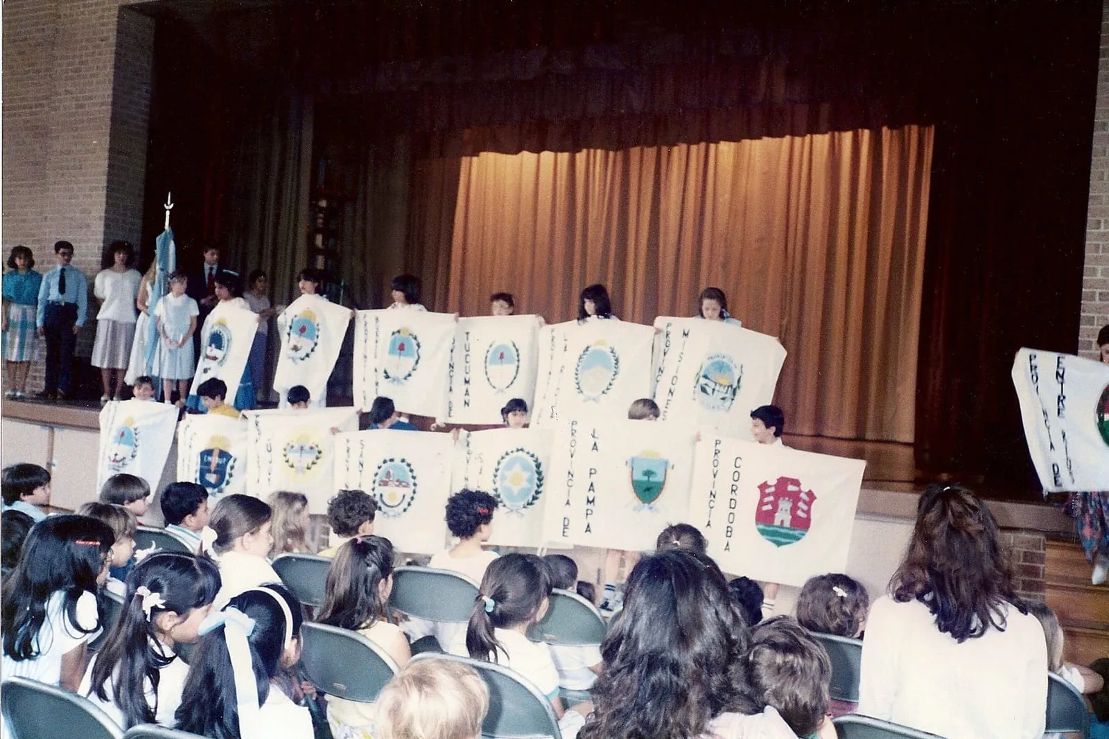 Estudiantes sosteniendo banderines con los escudos de las provincias argentinas durante un acto escolar.